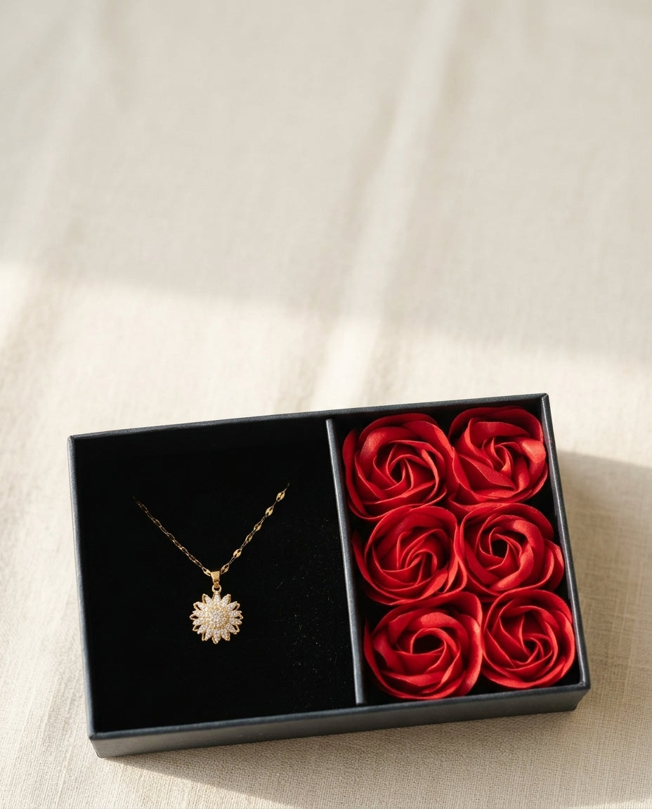 Caja de regalo abierta con el collar girasol dorado y seis rosas rojas sobre lino crema