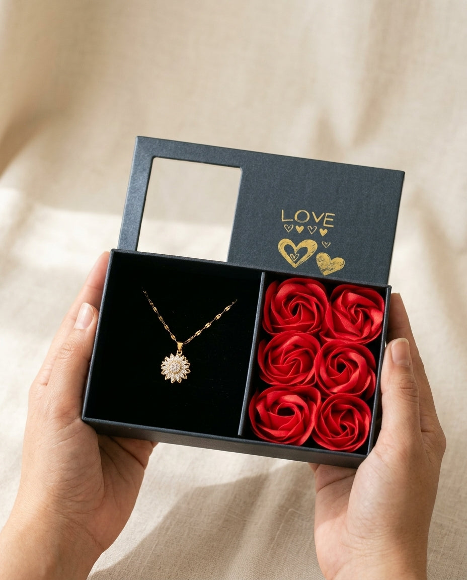 Dos manos sostienen la caja abierta con el collar girasol y las seis rosas rojas
